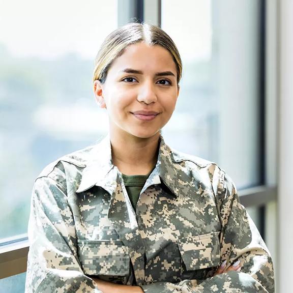 A confident female soldier stands with her arms crossed while working in a recruitment office.