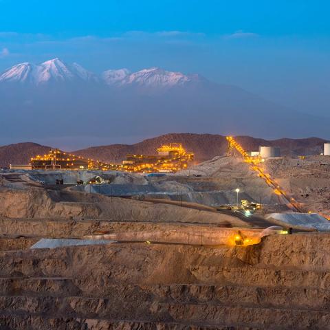 Un paysage montagneux au crépuscule, avec des opérations minières éclairées et des sommets enneigés en arrière-plan.