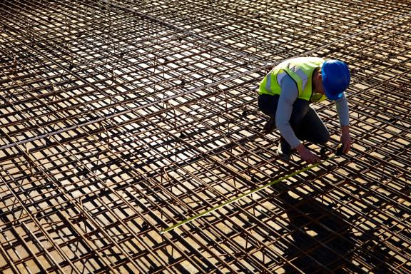 Builder measuring spacing of reinforcing rods laid down to prepare for concrete to be poured on to create a new floor on a large building site