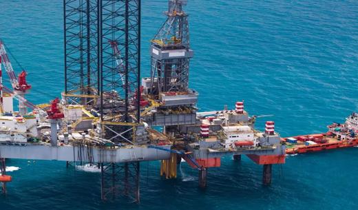 Offshore oil drilling platform with cranes, equipment, and support vessels in blue water.