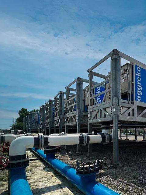 A low-angle shot of a long, blue industrial container unit on a tall, gray metal frame with several similar units fading into the background under a cloudy sky.