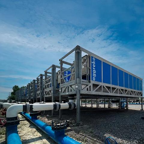 A low-angle shot of a long, blue industrial container unit on a tall, gray metal frame with several similar units fading into the background under a cloudy sky.
