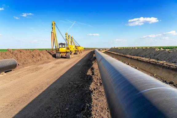 Heavy Machinery and Gas Pipeline Construction Site. Pipes are Laid on Top of Supportive Sandbags Beside Trench and Welded Together.