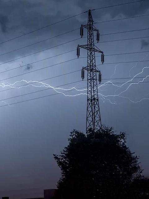 Vue d’un ciel gris et orageux traversé par des éclairs, avec la silhouette de pylônes électriques.
