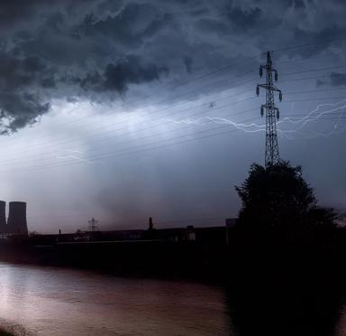 View of a grey, stormy sky with lightning the outline of transmission towers 