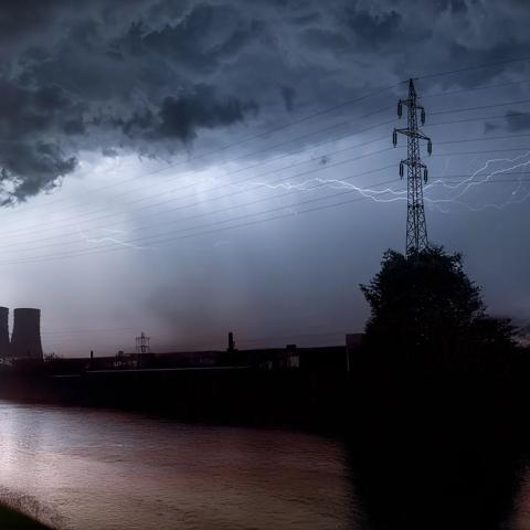 View of a grey, stormy sky with lightning the outline of transmission towers.
