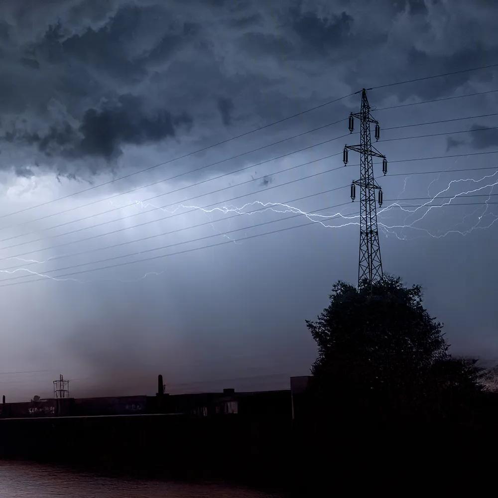 View of a grey, stormy sky with lightning the outline of transmission towers.