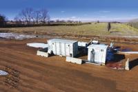 Two white and gray containerized industrial units sit on flat, brown terrain.