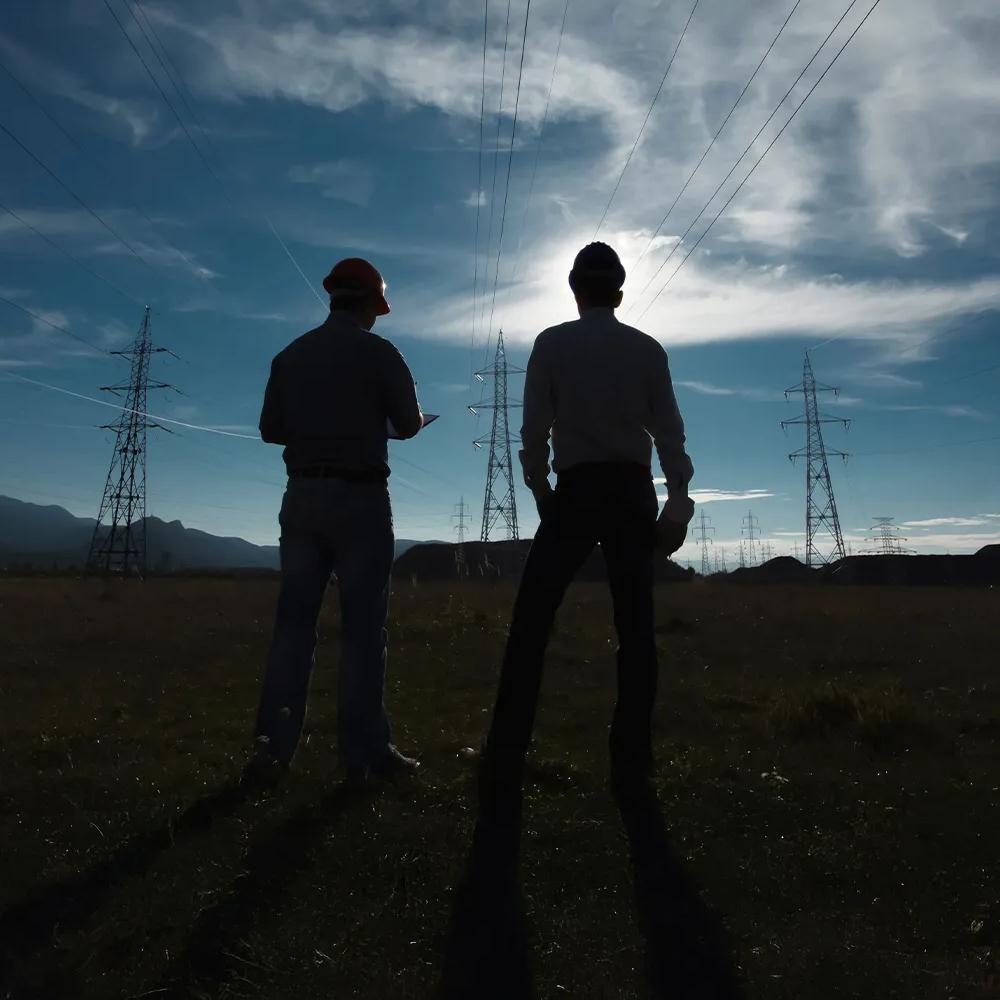 Shadow of two workers standing in a field seeing three main transmission towers and multiple towers in the background