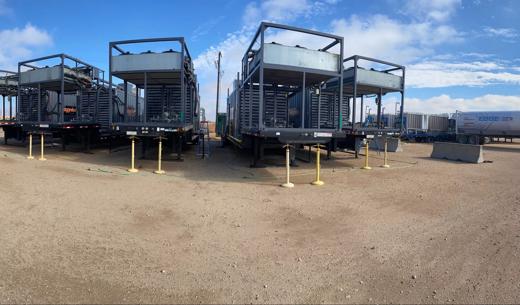 Four natural gas generators lined up on a gravel surface under a partly cloudy sky.