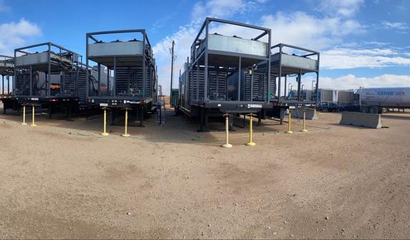 Four natural gas generators lined up on a gravel surface under a partly cloudy sky.
