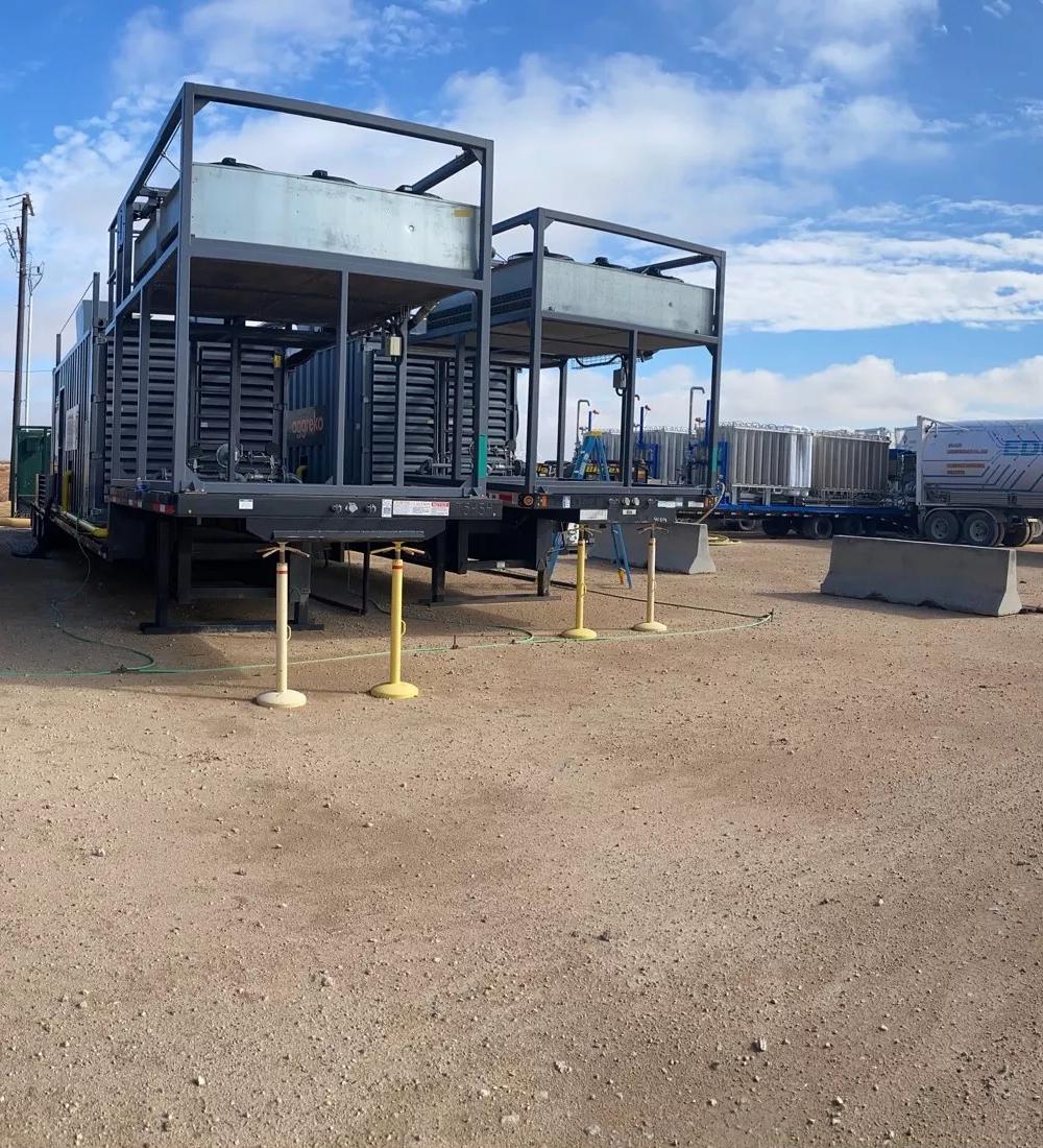Four natural gas generators lined up on a gravel surface under a partly cloudy sky