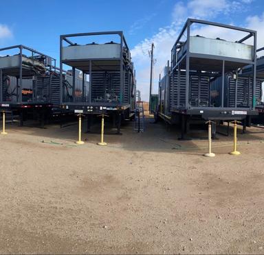 Four natural gas generators lined up on a gravel surface under a partly cloudy sky.