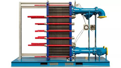 An industrial heat exchanger unit with exposed black plates, red tightening bars, mounted on a blue skid frame with connected blue piping, and yellow flanges.