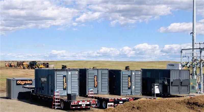 Multiple gray Aggreko industrial units in an open field.