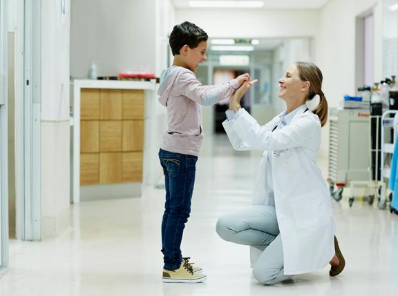 Full length side view of female doctor giving high-five to boy in hospital corridor