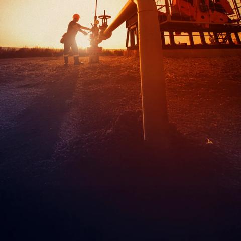 A worker next to an oil rig on a field against a sunset