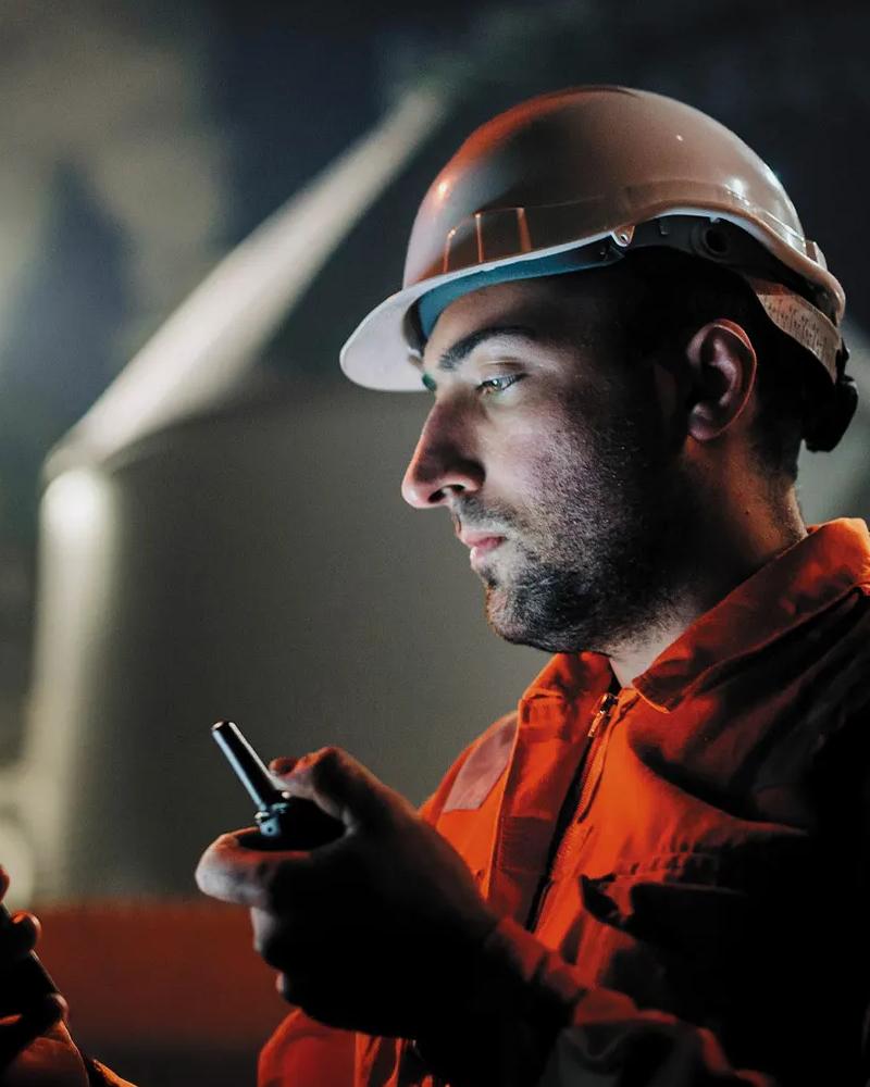 Worker in uniform looking at his phone whilst holding a walkie-talkie.