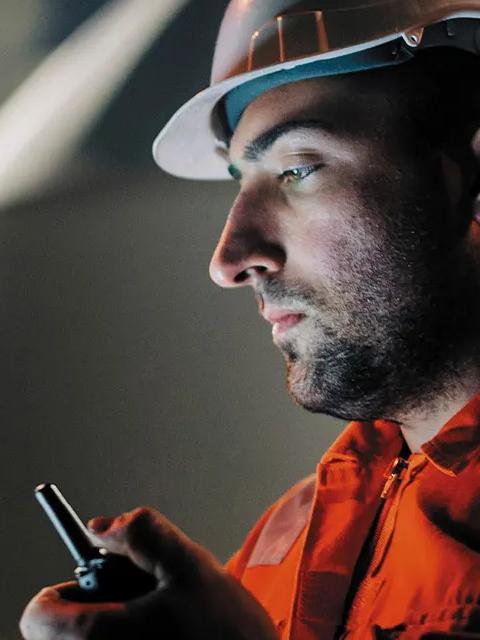 Gros plan sur un travailleur en uniforme regardant son téléphone tout en tenant un talkie-walkie.