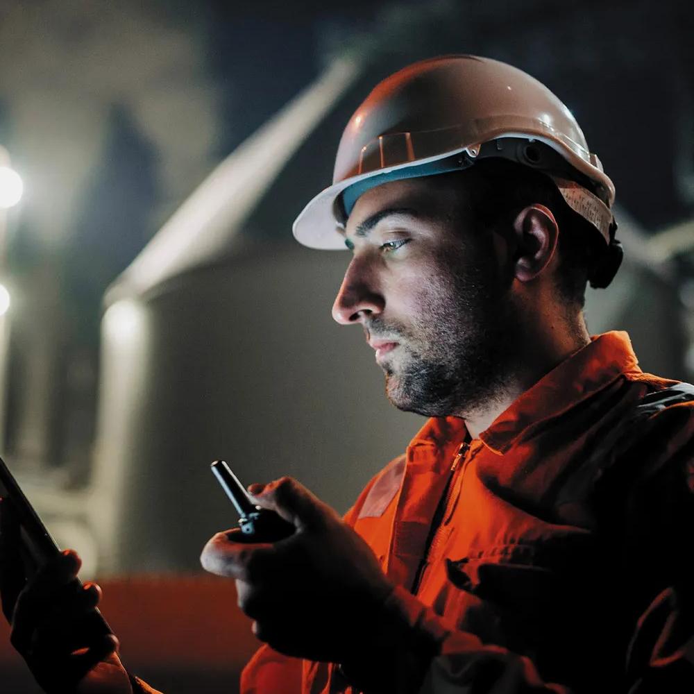 Close-up view of a worker in uniform looking at his phone whilst holding a walkie-talkie