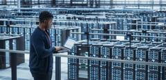 Data Center Engineer Using Laptop Computer. Server Farm Cloud Computing Specialist Facility with African American Male System Administrator Working with Data Protection Network for Cyber Security.