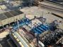 Aerial view of an industrial facility with blue machinery, storage containers, and various equipment on a large concrete area.