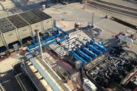 Aerial view of an industrial facility with blue machinery, storage containers, and various equipment on a large concrete area.