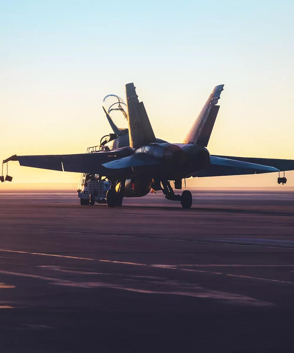 Vue extérieure en contre-plongée d’un avion de chasse militaire, stationné sur une piste au coucher du soleil avec la verrière ouverte.