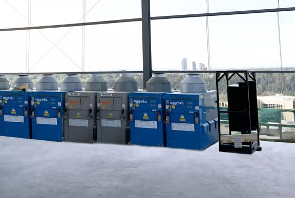 A row of blue and grey Aggreko heaters inside a building against a glass window