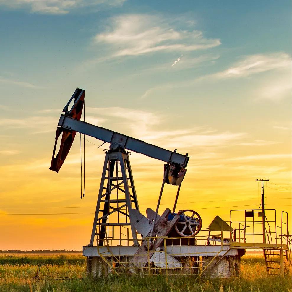 An oil pump jack stands against a backdrop of rolling green hills and distant mountains under a clear sky.