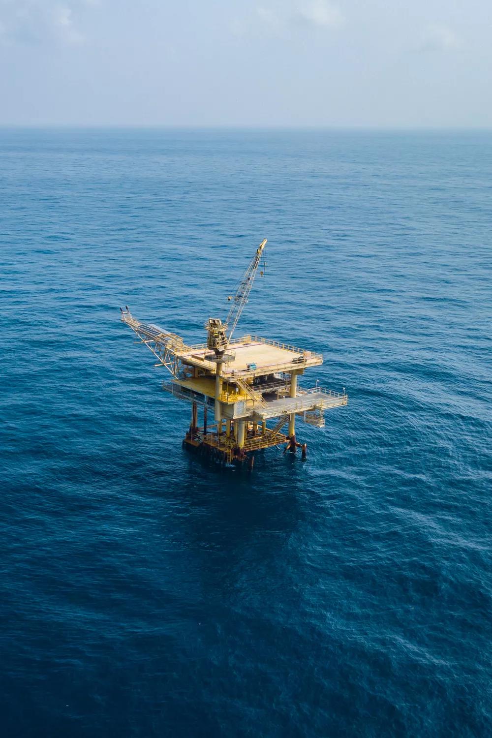 An aerial wide view of a small, fixed offshore oil platform resting in deep blue water.