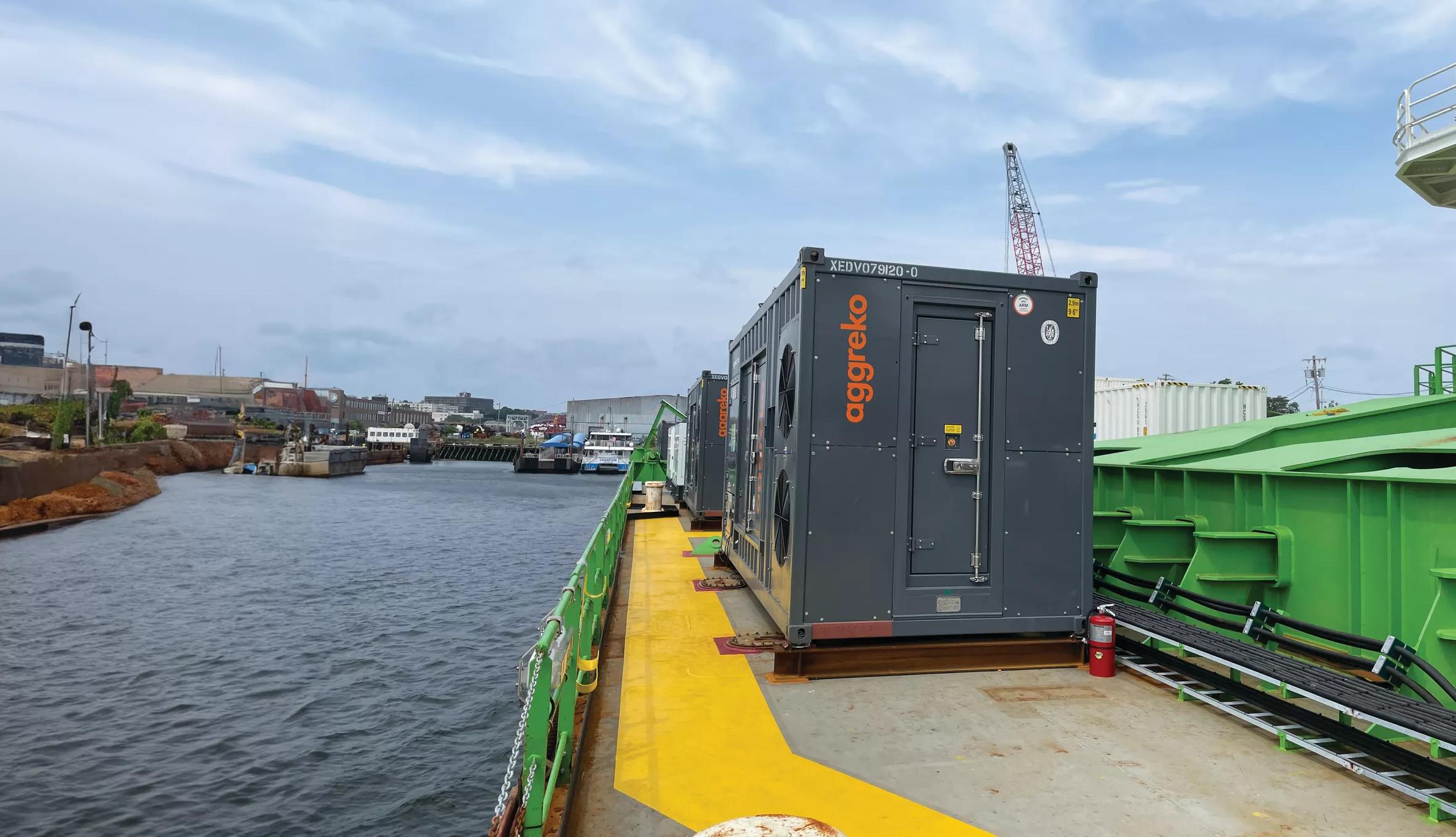 A large grey generator on a barge on a river
