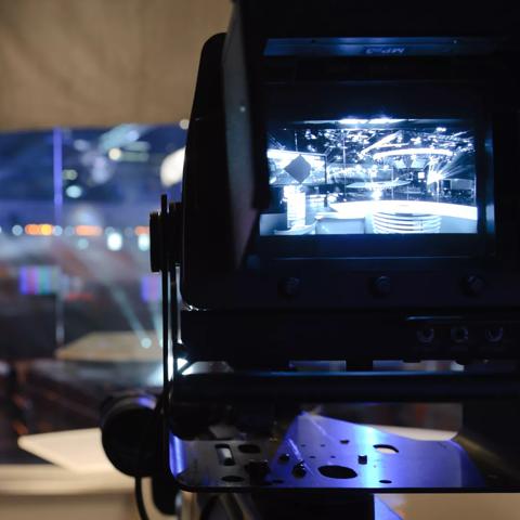 Professional video camera broadcasting several monitors in the background.