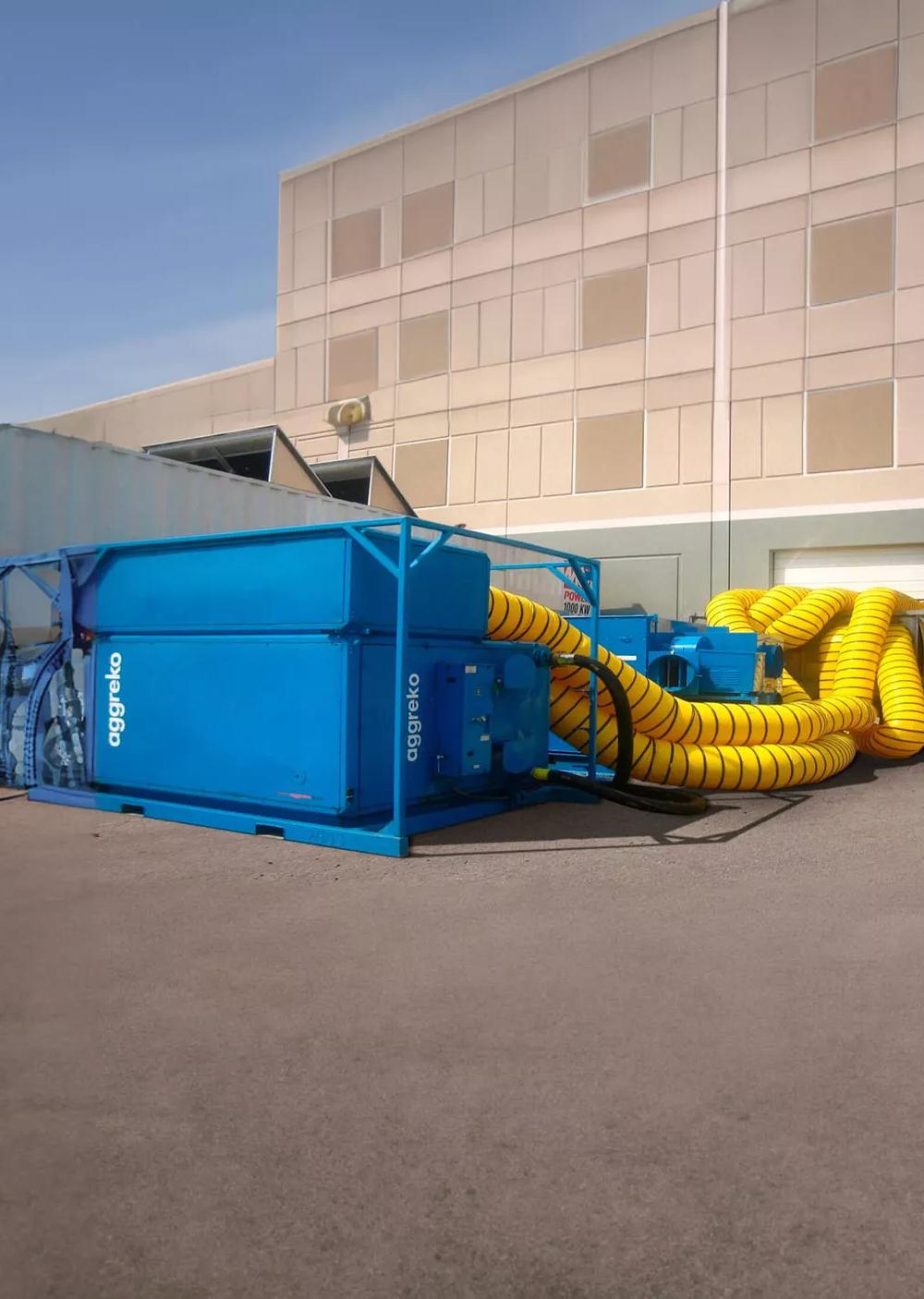 Blue Aggreko industrial unit with yellow hoses out the back, outside a facility.