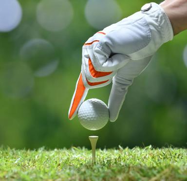 Hand wearing golf glove, placing golf ball on tee.