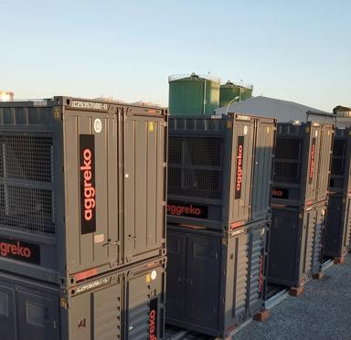 Close-up view of a row of multiple dark gray Aggreko industrial units stacked.
