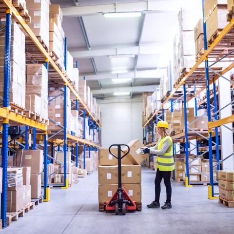 Young female warehouse worker loading up a pallet truck with boxes.