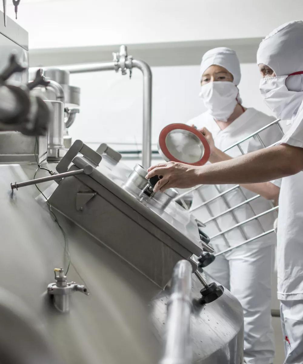 Un travailleur en combinaison blanche et masque facial se penche sur un équipement industriel.