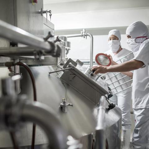 A worker in a white sanitary suit and face mask is leaning over industrial equipment.