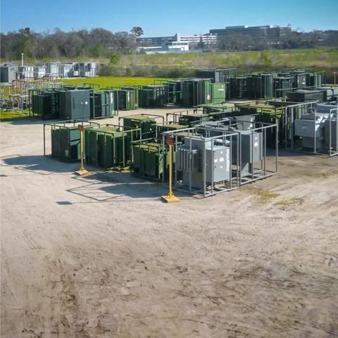 View of multiple Aggreko grey transformers amongst other green equipment at a worksite 