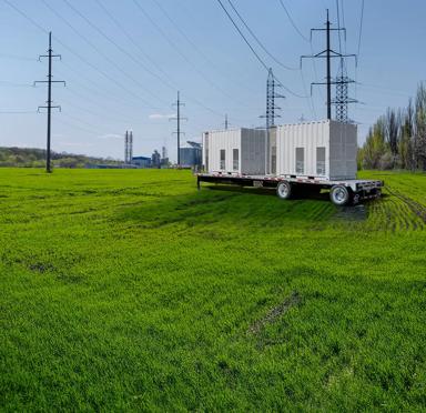 Transformer in a field with a power plant in the background.