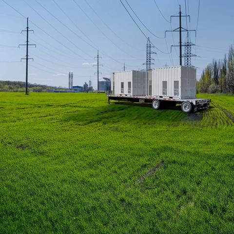 Transformer in a field with a power plant in the background.