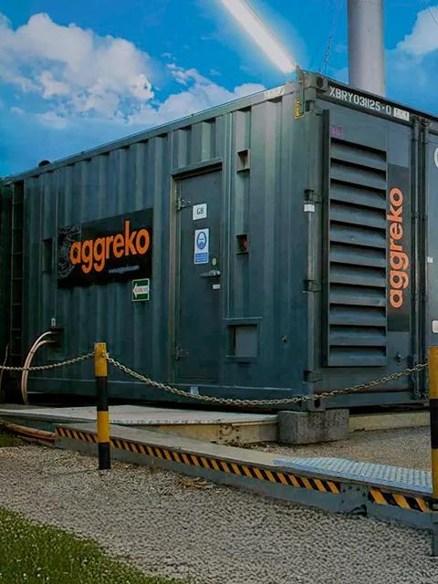 Vue rapprochée d’une rangée de conteneurs industriels noirs d’Aggreko sur un terrain de gravier