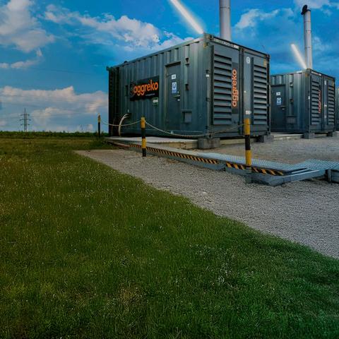 Close-up view on a row of black Aggreko industrial containers on a gravel field
