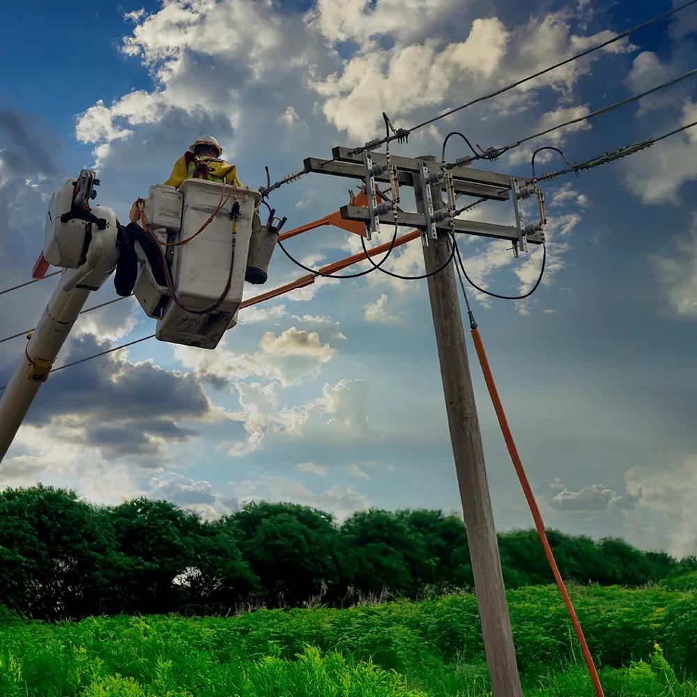 Ground view of a worker in uniform checking a power line.