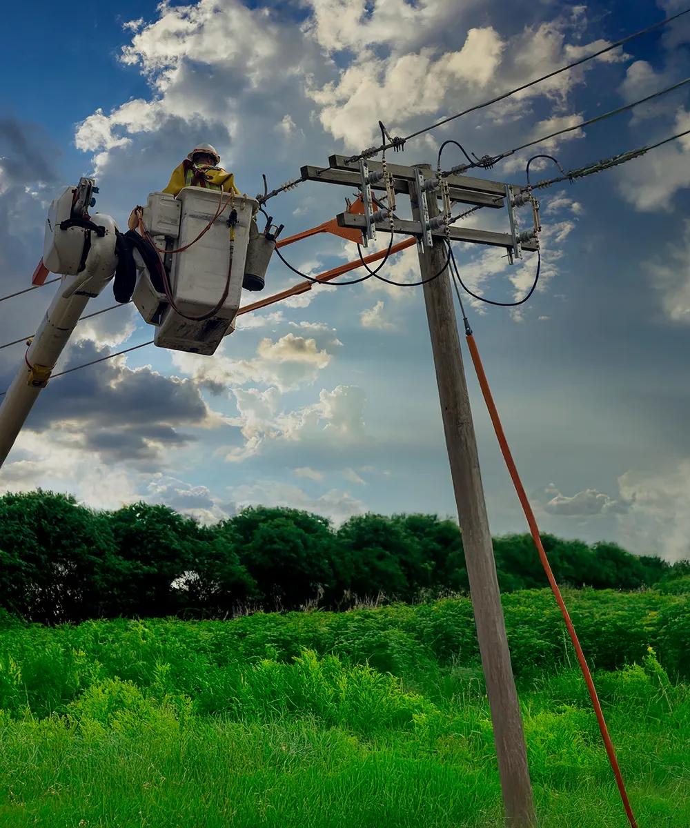 Ground view of a worker in uniform checking a power line.