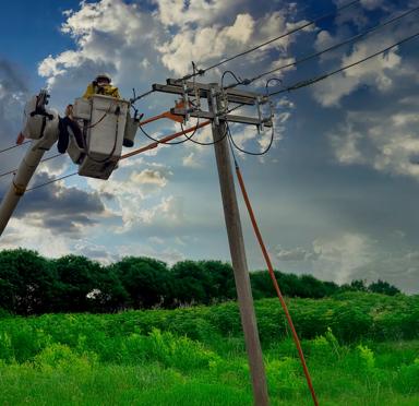 Ground view of a worker in uniform checking a power line.
