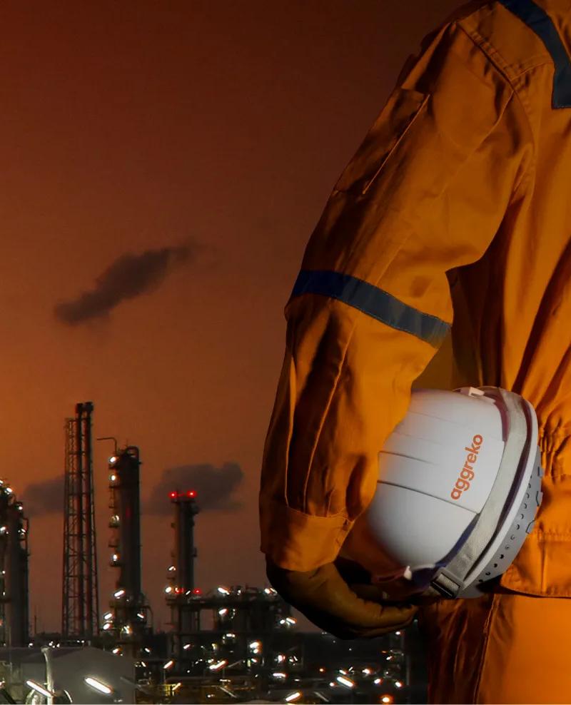 Aerial view of a lit-up refinery at night during an orange sunset.