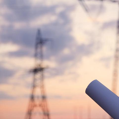 Un électricien travaillant dans une centrale électrique à haute tension consulte un dossier de projet au coucher du soleil.
