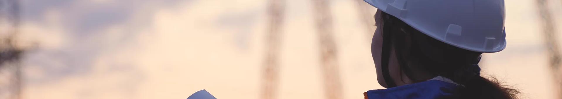 An electrician at a high voltage power plant works with a project folder at sunset.